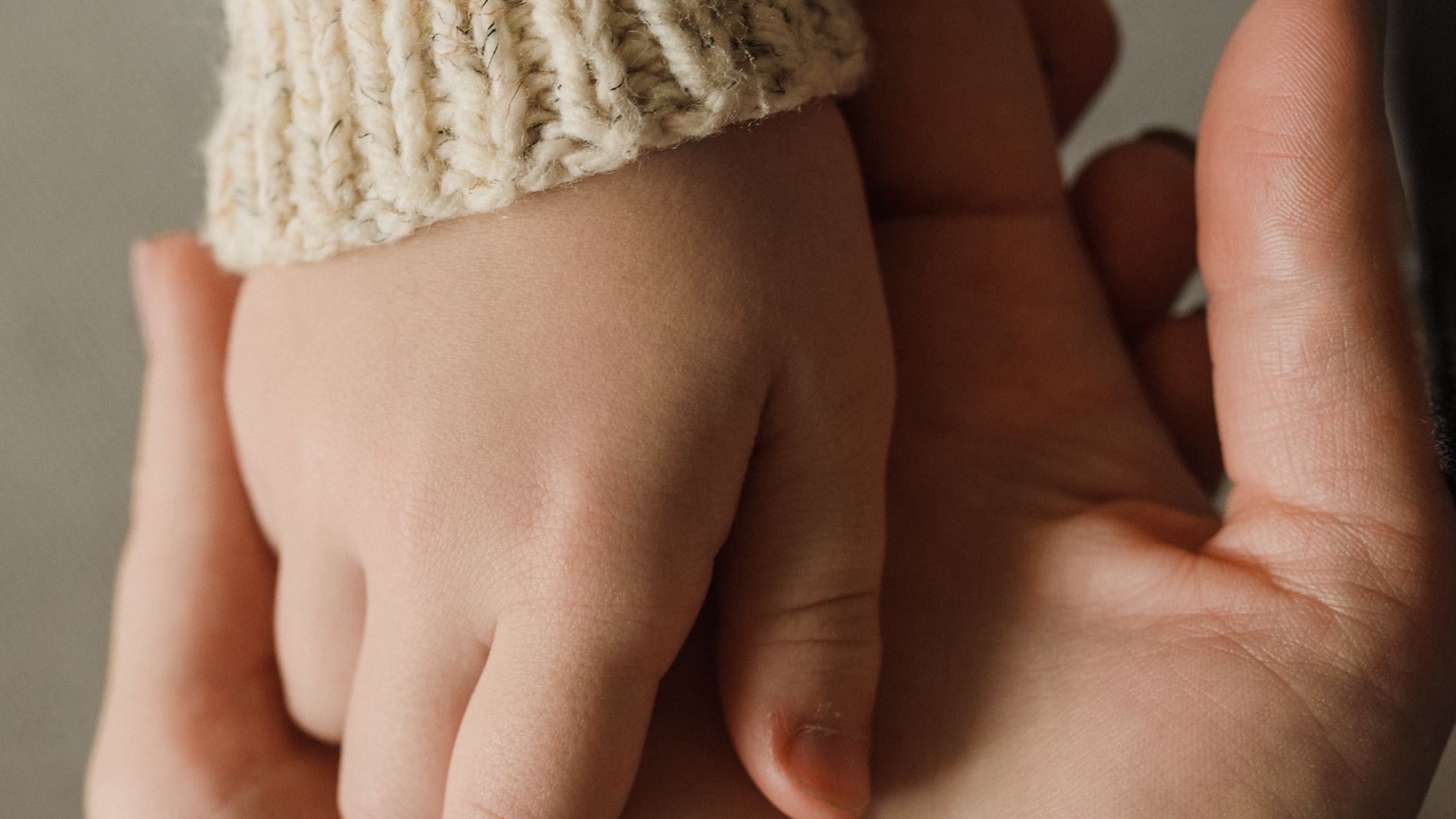 A mother's hand cradling her toddler's small hand, close up