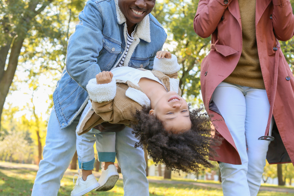 Two parents laughing as they swing their toddler outdoors