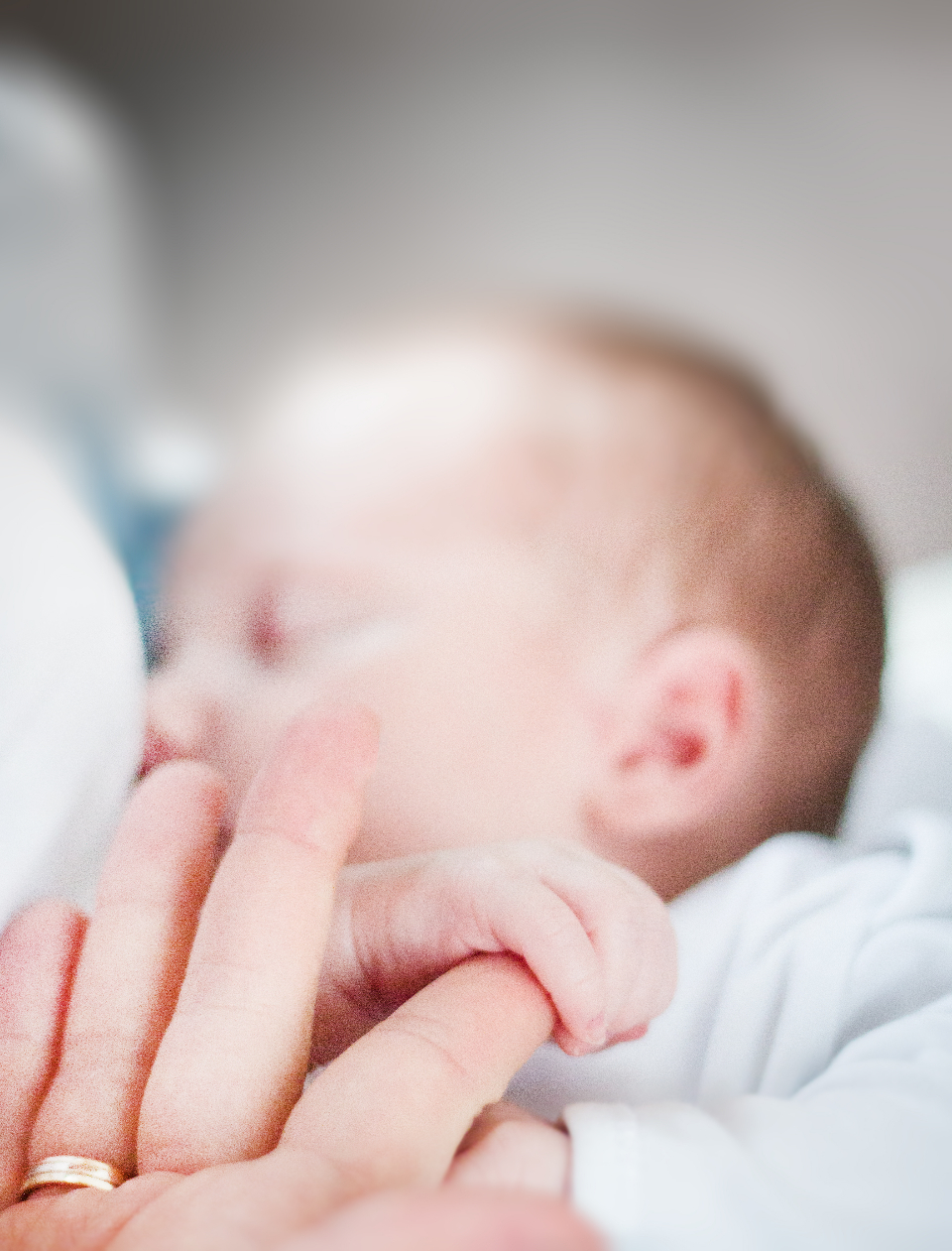 An adult's hands cradling a sleeping newborn